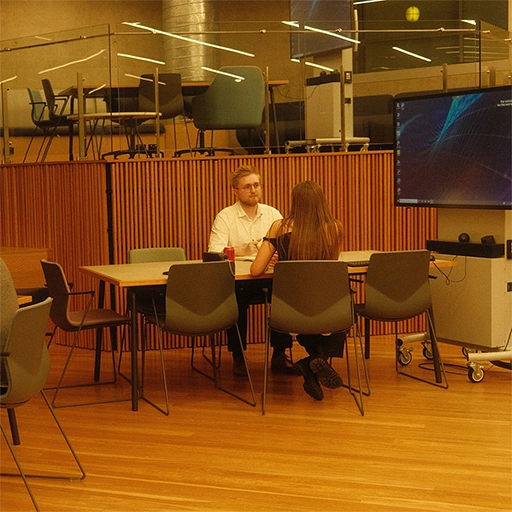 A man and a woman sitting at a table in a lecture hall talking.
