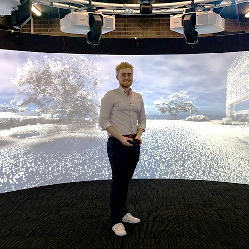 Man standing holding a game controller infront of a 360 degree immersive display.