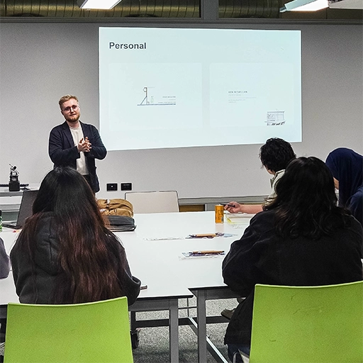 Man presenting infront of a projector screen with people sitting in front.